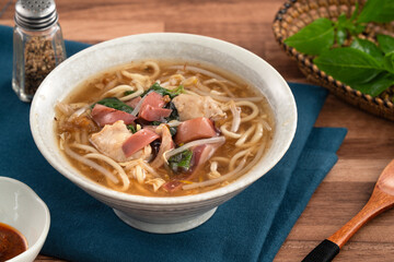 Taiwanese squid thick noodle soup in ceramic bowl on wooden table background.