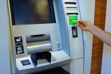 A person inserts a bank card into an ATM slot, initiating a secure banking transaction. Closeup of...