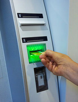 A person inserts a bank card into an ATM slot, initiating a secure banking transaction. Closeup of a client hand inserting a card into an cash machine terminal for money withdrawal