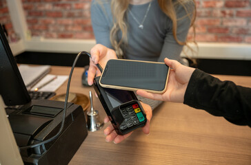 Hand of young woman holding smartphone close to electronic payment machine 