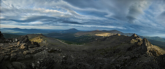Breathtaking vista showcases rugged terrain interspersed with shadows and light as storm clouds drift across the sky during twilight in a mountainous area