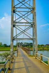 a towering suspension bridge tower with an iron frame structure against a clear sky backdrop for advertising space. A steel suspension bridge spans a river flanked by greenery under a bright blue sky.