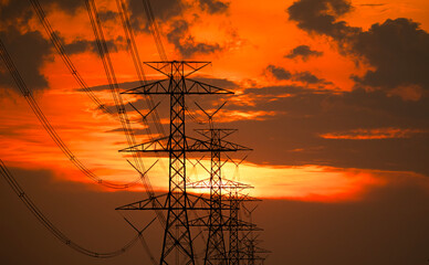 Silhouette of high-voltage electric pole with red-orange clouds during sunset.