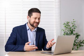 Smiling online speaker streaming webinar with laptop at table indoors