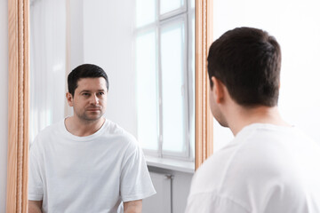 Handsome man looking at himself in mirror indoors