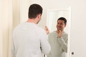 Handsome man showing heart gesture near mirror indoors