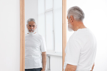 Obraz premium Handsome senior man looking at himself in mirror indoors