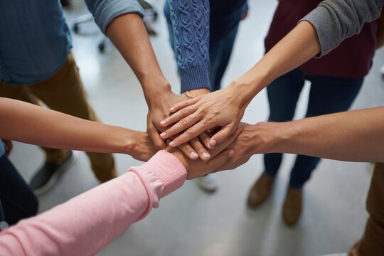 Group of diverse people standing in a circle with hands stacked in the center symbolizing teamwork and unity - Powered by Adobe