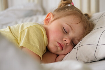Peaceful adorable baby sleeping on a bed at home. Slumbering little child. Two years old girl sleeps peaceful at domestic room interior background. Serene dream. Cute face close up. Deep kid slumber