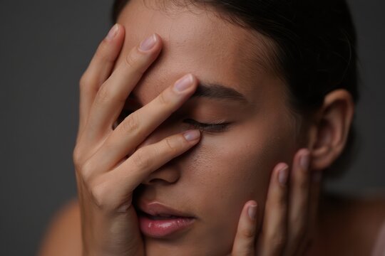Close-up portrait of a young person with eyes closed covering part of the face with one hand and resting the other hand on the cheek expressing contemplation or calmness