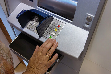 Senior Hand Using ATM. Keypad. A closeup of a person hand pressing the green button on an ATM keypad while withdrawing or managing money.
