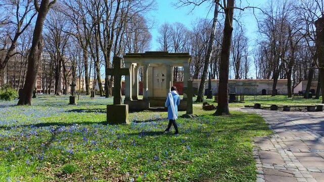 Young woman walks peacefully, Riga historic Lielie Kapi under spring trees