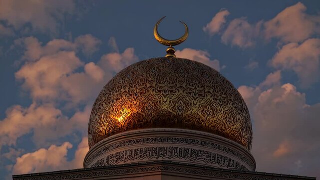 Low-angle video shot of a mosque dome with intricate patterns, glowing in sunset light against a backdrop of soft, scattered clouds. Live desktop wallpaper.