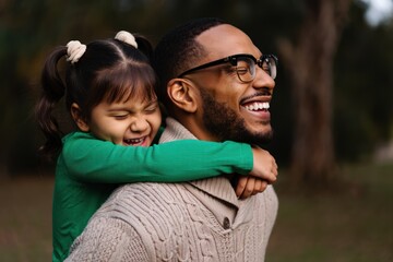 Obraz premium Joyful young girl hugging smiling bearded man from behind outdoors in cozy sweater and green top expressing happiness and love
