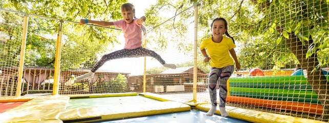 Pretty girls jumping together on colorful trampoline at playground park. Two sisters having fun during active entertainments 