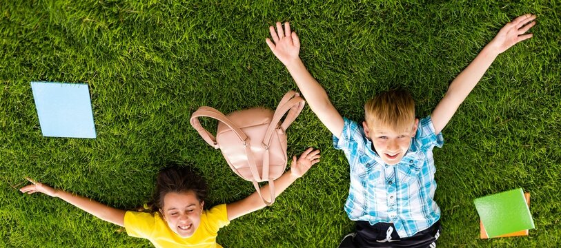 Happy peaceful childhood. Two happy little children - a boy and a girl in summer clothes are lying on a green lawn in a summer park. Summer kids fashion. Summer holidays, vacation. 