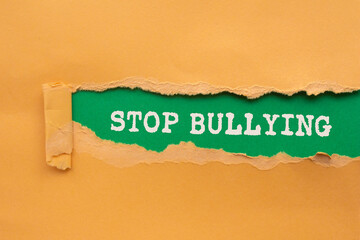 Stop bullying message written on ripped torn orange paper on green background. Conceptual stop...