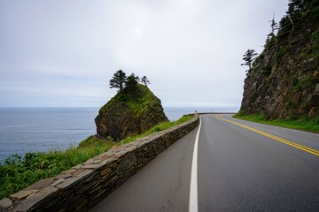 Curved coastal road with stone wall overlooking ocean and rocky cliffs under cloudy sky