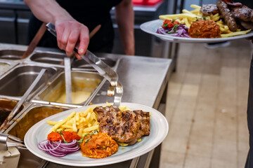 Chef serving rice and vegetable stew onto plates with red pepper relish and sliced onions in a restaurant kitchen. Food prep in progress at a buffet-style serving station.