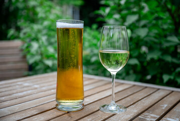 Cold beer and white wine glass on wooden table outdoors in summer garden