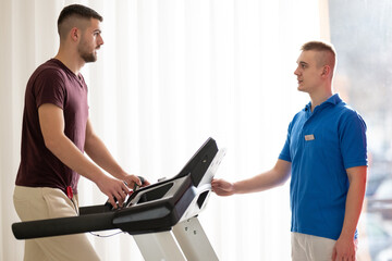 Physical Therapy on Treadmill.Man undergoing physical therapy with trainer assistance on a...