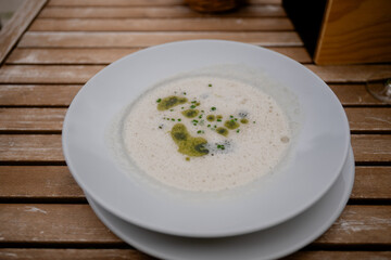 Creamy gourmet mushroom soup with herb oil on rustic wood table outdoors, concept of outdoor dining