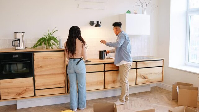 A man turns on a lamp while talking to a woman who is washing her hands next to him and wiping them with a napkin while he opens a drawer
