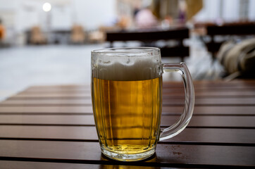 Cold beer mug with foam on wooden table in outdoor seating area of a pub