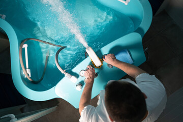 Spa Therapist Adjusting Tub. A therapist preparing a hydrotherapy bathtub for a patient inside a tiled wellness room.
