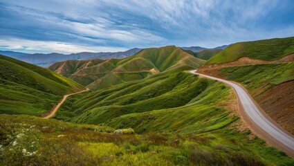 Winding road through lush green rolling hills under a partly cloudy blue sky with distant mountain range