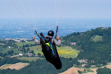 Sestola, Italy – 05 31 2025: Paraglider flies in the air. Aerial view of paragliding. Paraglider flies above the mountains in a bright sunny day. Concept of extreme sport.

