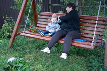 Grandmother and grandchild share a quiet moment on an old wooden swing amidst a verdant garden,...