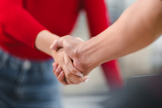 Two people shaking hands in close up, symbolizing agreement, partnership, or successful business deal, with one person wearing red sweater and other in casual attire