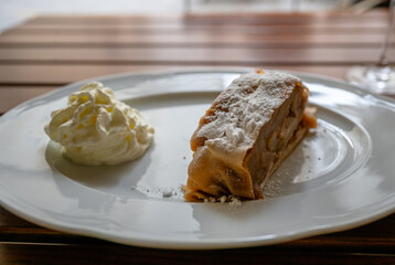 Apple strudel slice with whipped cream on white plate on wooden table surface