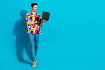 Young man in vibrant shirt using laptop against blue background, showcasing style, fashion, and...
