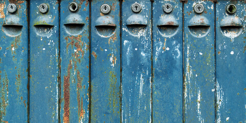 Row of vintage blue metal mailboxes with weathered surfaces, rusty spots and peeling paint creates nostalgic urban atmosphere.