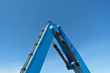 Closeup of blue hydraulic excavator arm against clear sky highlights industrial power, engineering...