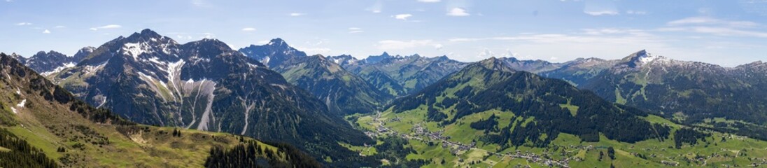 Ein weitl&auml;ufiges Bergpanorama mit gr&uuml;nen T&auml;lern unter einem teils bew&ouml;lkten Himmel mit Blick auf die D&ouml;rfer Hirschegg, Riezlern und Mittelberg im Kleinwalsertal, &Ouml;sterreich, Europa