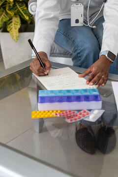 Doctor writing prescription for patient at home visit with pills and pillbox on table
