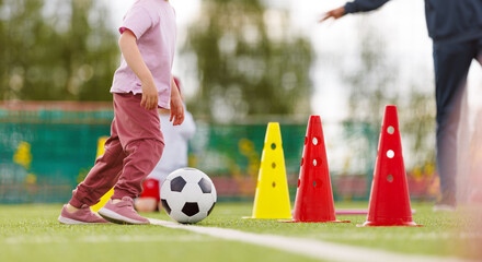 Fototapeta premium Little Girl Practicing Soccer Dribbling Skills on Sports Field with Colorful Training Cones and Coach Supervision
