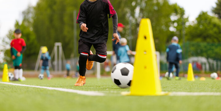 Young Soccer Player Dribbling Ball Through Yellow Training Cones During Youth Practice on Outdoor Field - Powered by Adobe