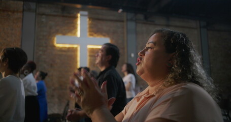 Woman clapping with joy during worship in church, glowing cross in background, heartfelt expression...