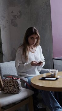 girl sits at a coffee shop table and surfs phone