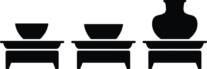 Three black silhouette illustrations of bowls and a vase on stands against a white background space
