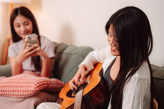 Asian Woman Music Guitar Playing Togetherness Song Teenage Indoor Living Room, Joyful Gathering of Friends Sharing Music, Laughter, and Relaxation Through Guitar Playing at Home