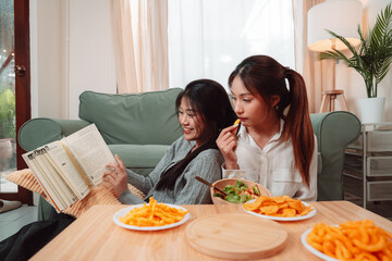 Asian Women Snack Food Eating Lifestyle Indoor Living Room Enjoyment Movie, Two Young Adults Sharing Laughter and Snacks While Watching TV, Embracing Friendship and Relaxation at Home Together