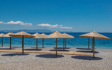 straw umbrella on a beach of white pebbles n Peloponnese, Greece with their well drawn shadow in front beautiful sea