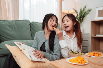 Asian Women Snack Food Eating Lifestyle Indoor Living Room Enjoyment Movie, Two Young Adults Sharing Laughter and Snacks While Watching TV, Embracing Friendship and Relaxation at Home Together