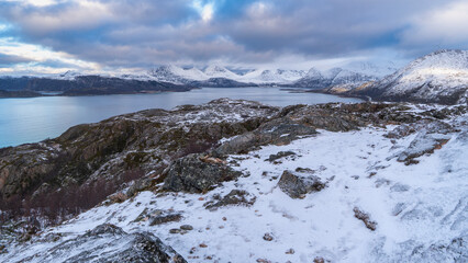 impressive, changing weather moods on the fjord between steep, snow-covered mountains around the island Kvaloya in Troms, Norway. Panorama with sea, dark clouds on the sky and snowy mountains