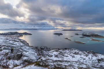 impressive, changing weather moods on the fjord between steep, snow-covered mountains around the island Kvaloya in Troms, Norway. Panorama with sea, dark clouds on the sky and snowy mountains